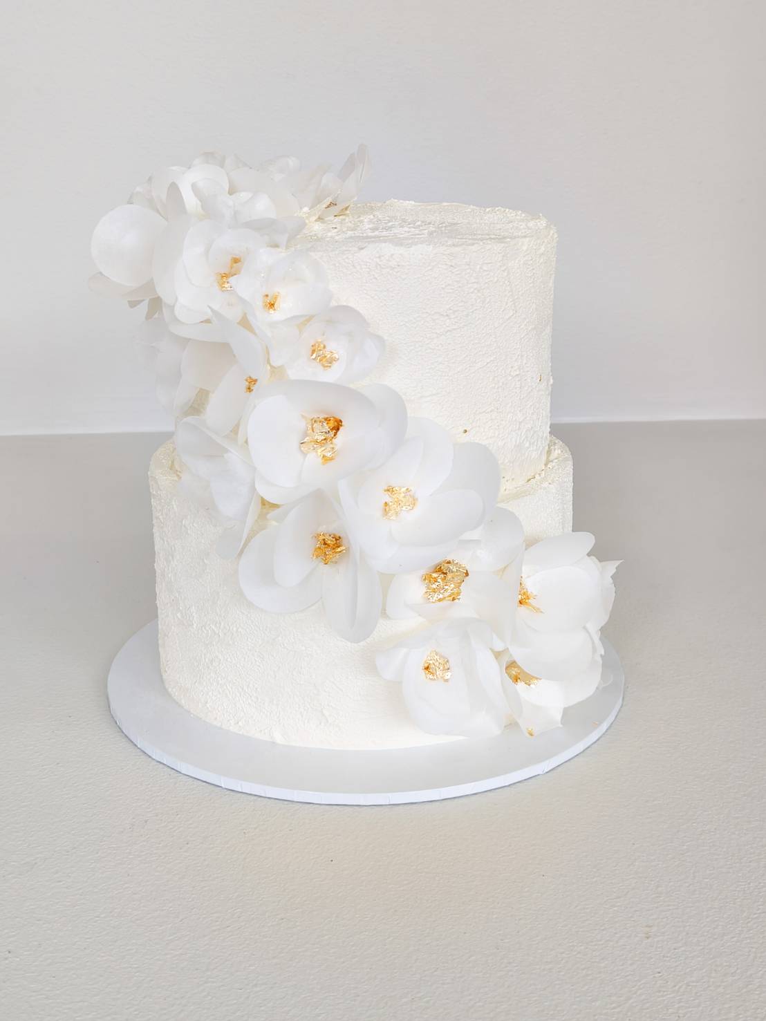Two-tier luxury white wedding cake decorated with elegant white orchids and gold accents. Perfect for weddings and elegant celebrations.
