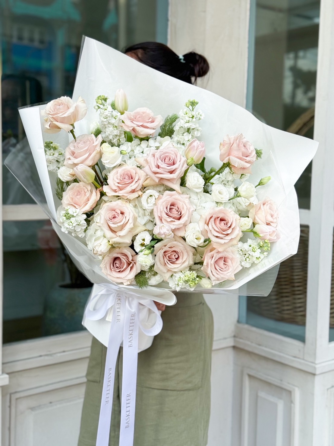 Large luxury bouquet with pastel pink roses, white lisianthus, and white accent blooms, wrapped in white paper with satin Basketeer ribbon.