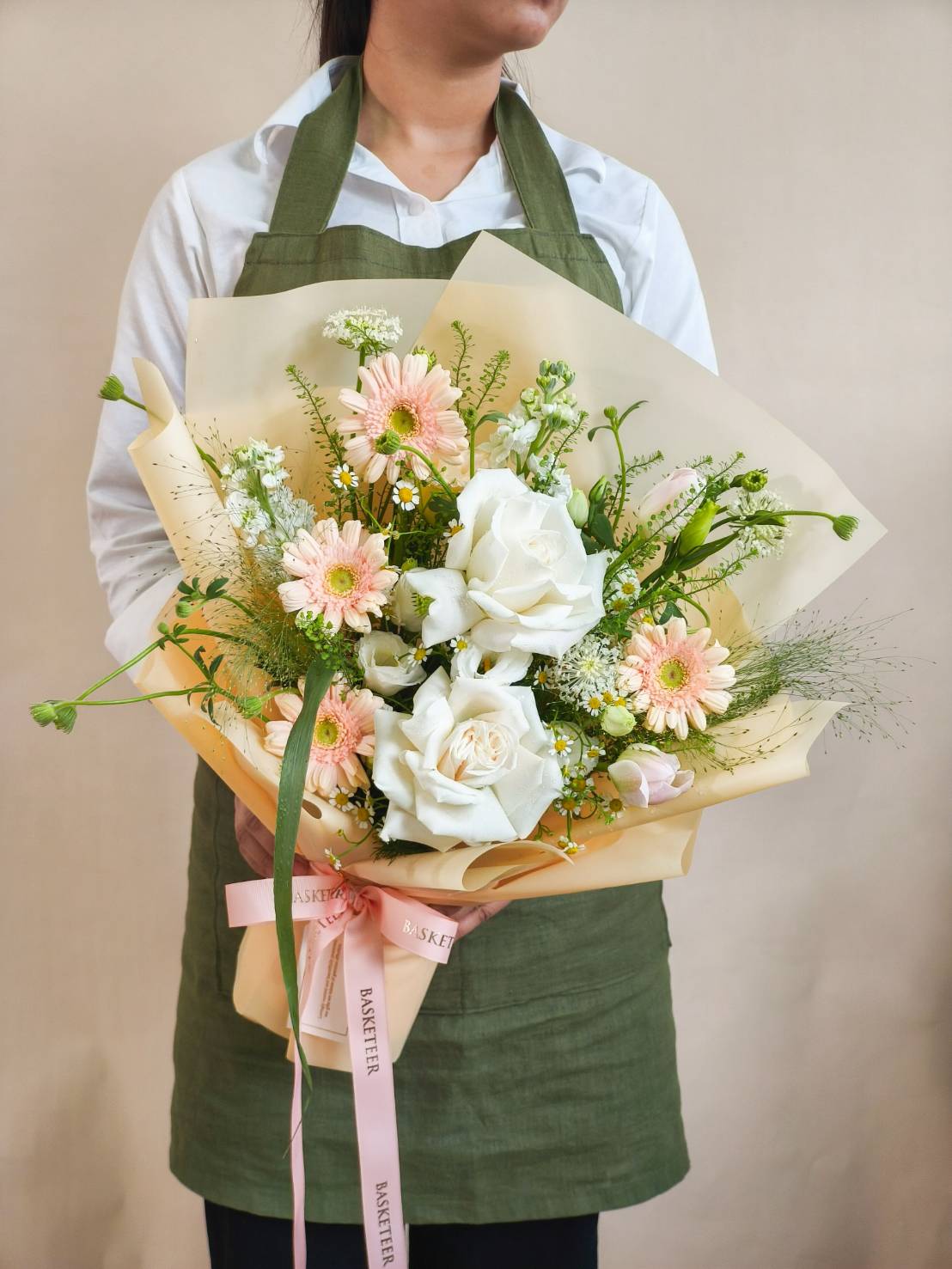 Elegant bouquet with white roses, peach gerbera daisies, and fresh greenery, wrapped in cream paper with pink satin ribbon
