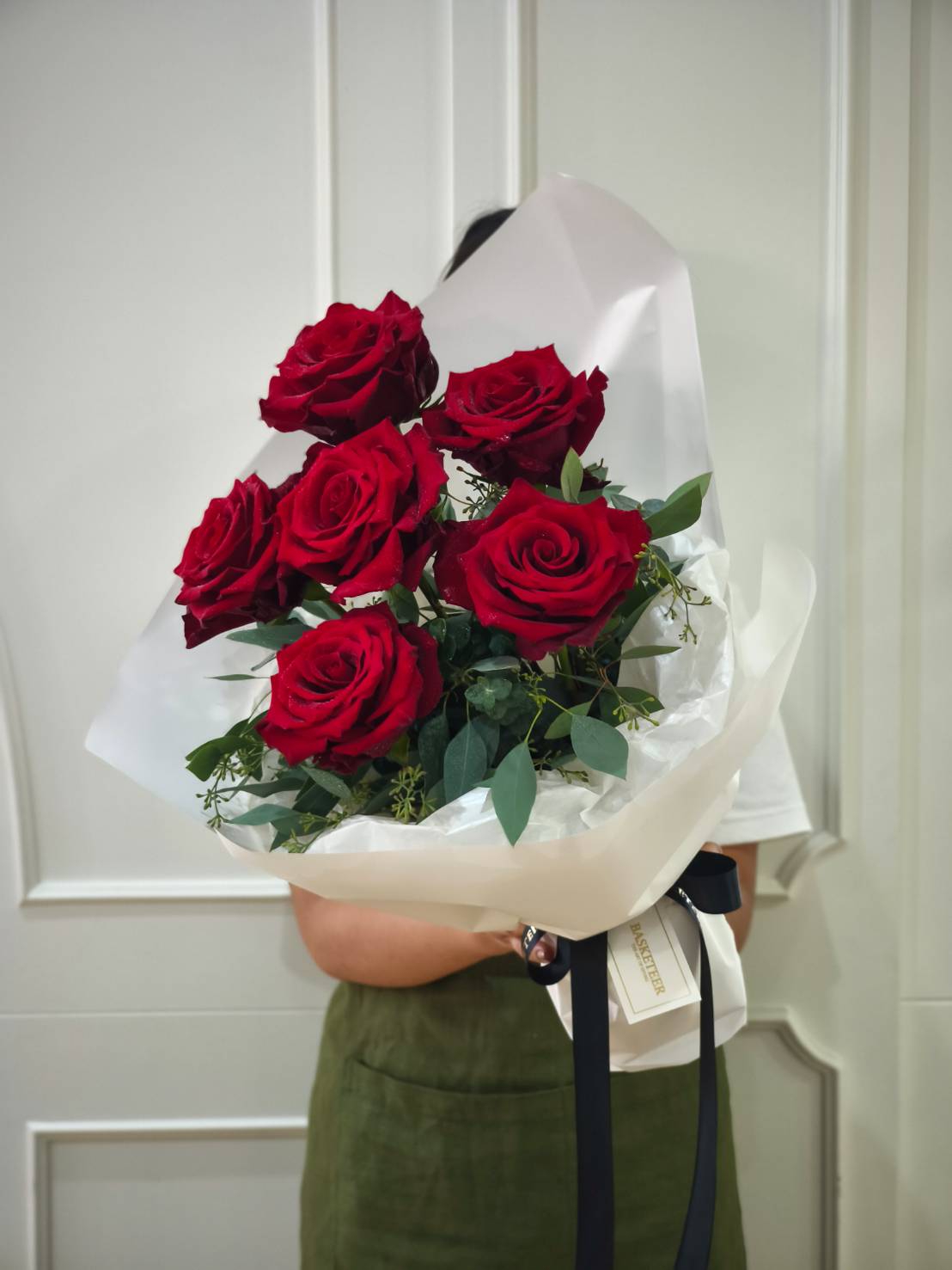 Elegant bouquet of six fresh red roses wrapped in white paper with black ribbon.