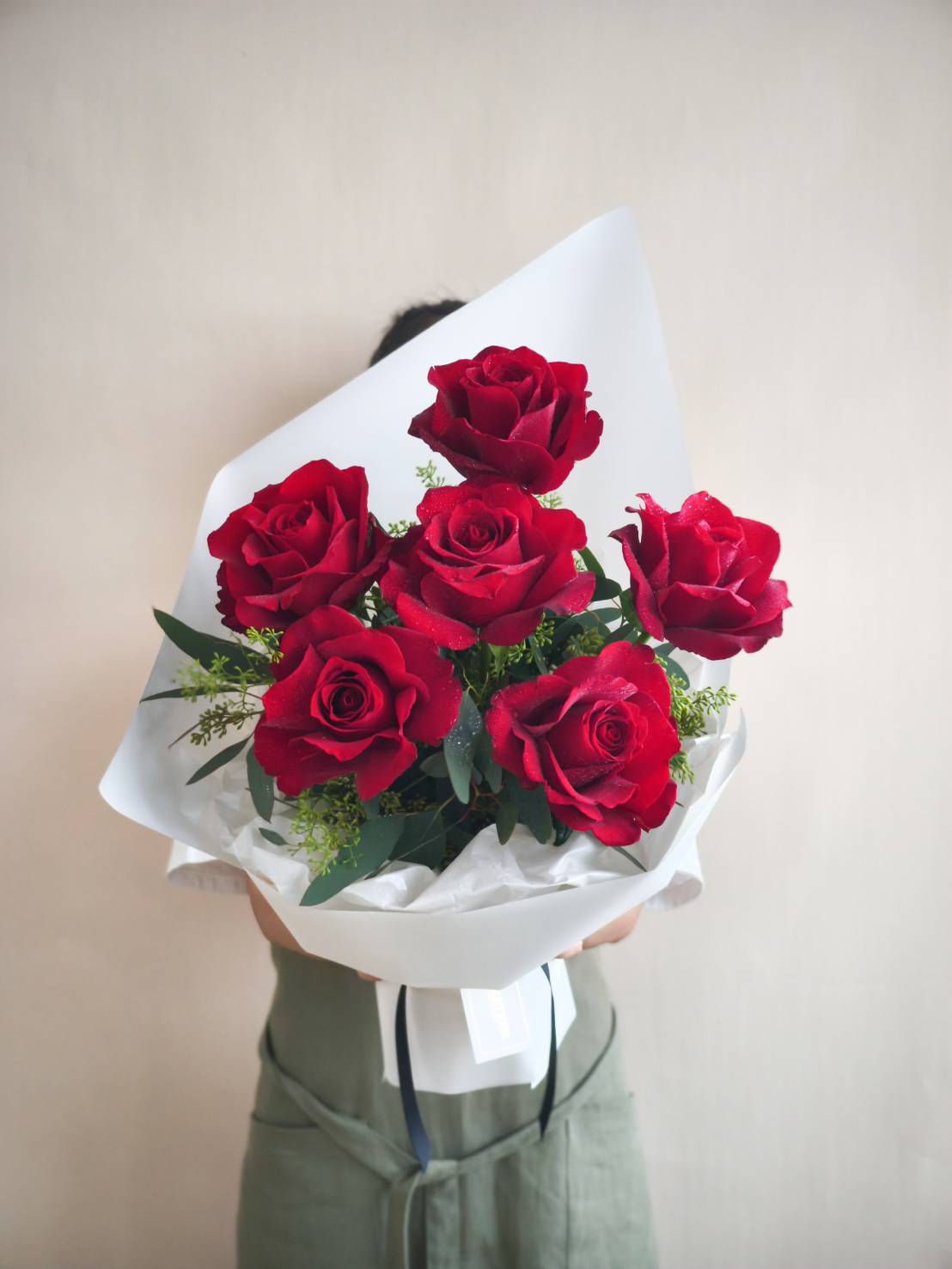 Elegant bouquet of six red roses with greenery, wrapped in chic white paper and tied with ribbon.