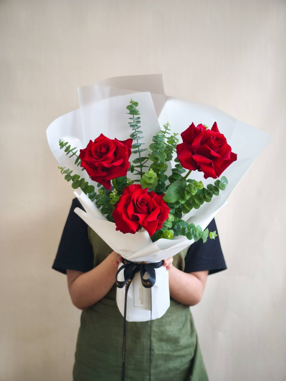 Three red roses bouquet with eucalyptus, wrapped in white paper and black ribbon