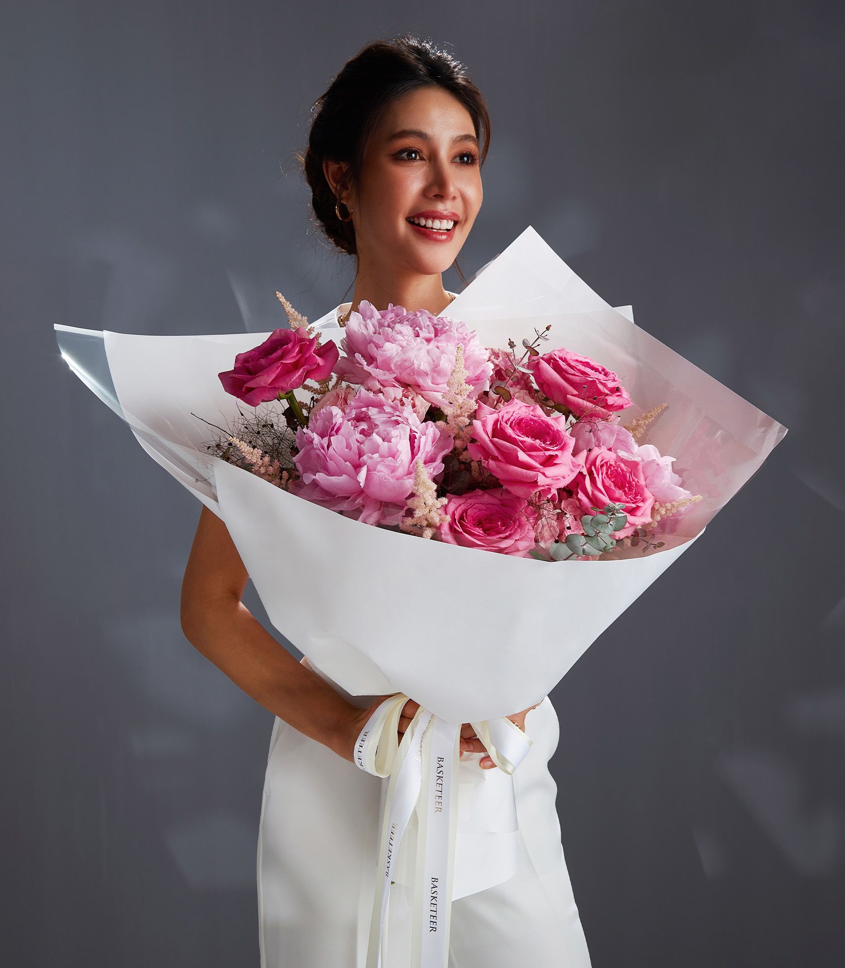 Smiling woman holding luxury bouquet of Nuage roses, pink peonies, hydrangeas, and blush astilbe with white wrapping