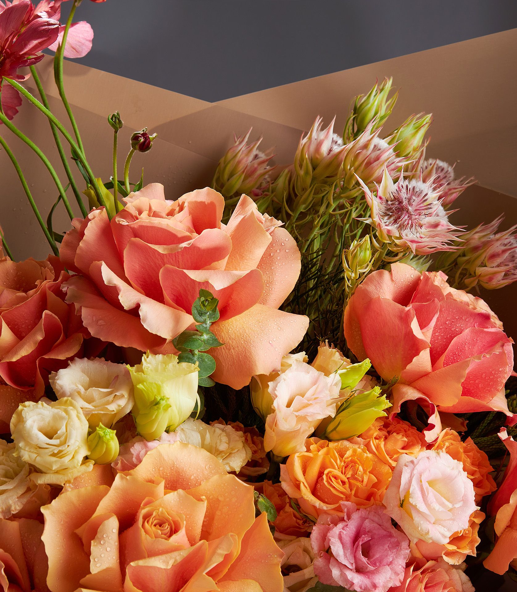 Bouquet of Tiffany roses, Butterfly ranunculus, spray roses, lisianthus, and Blushing Bride protea in warm peach and coral tones.