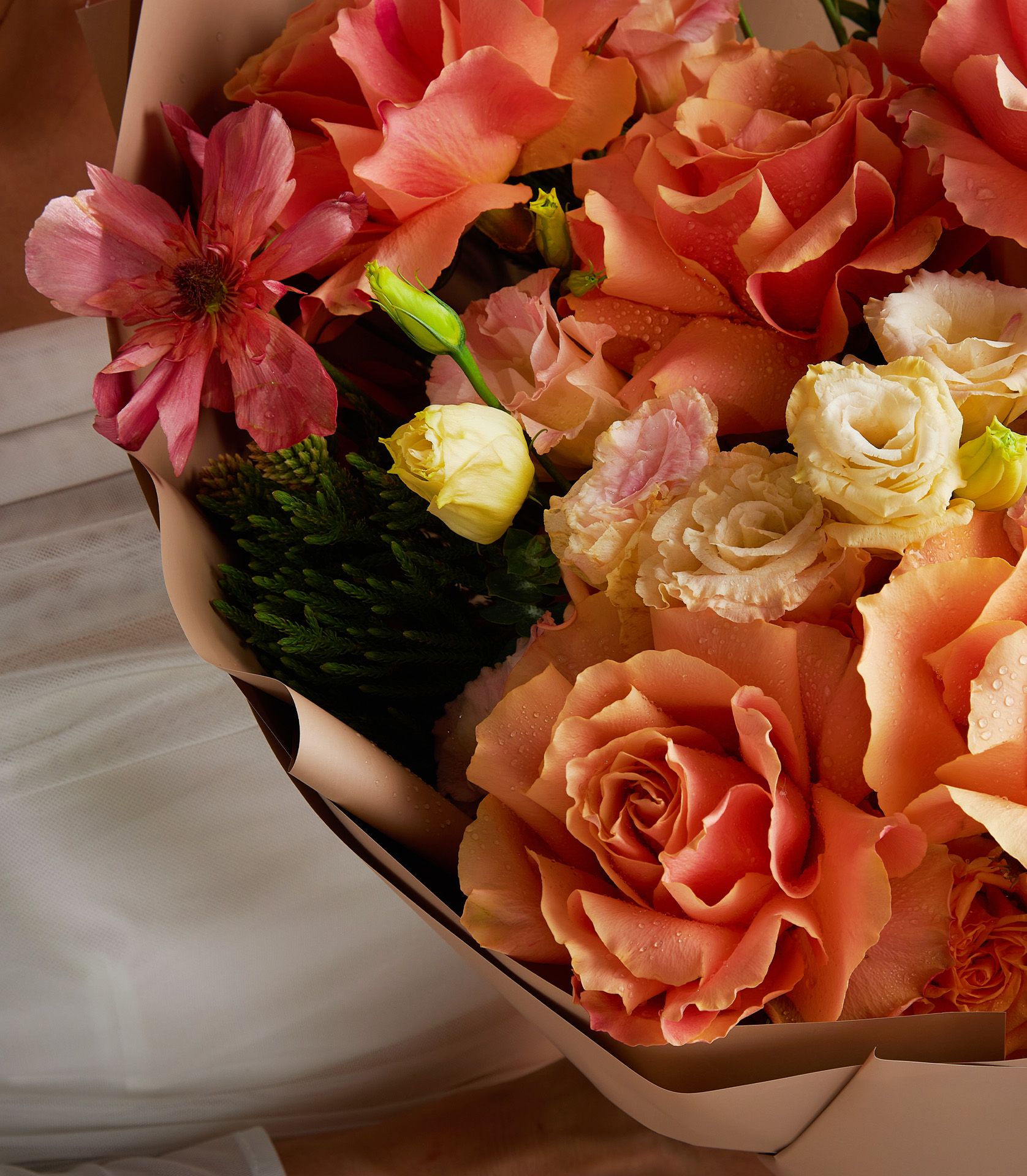 Close-up of bouquet with Tiffany roses, butterfly ranunculus, yellow lisianthus, spray roses, and Blushing Bride protea