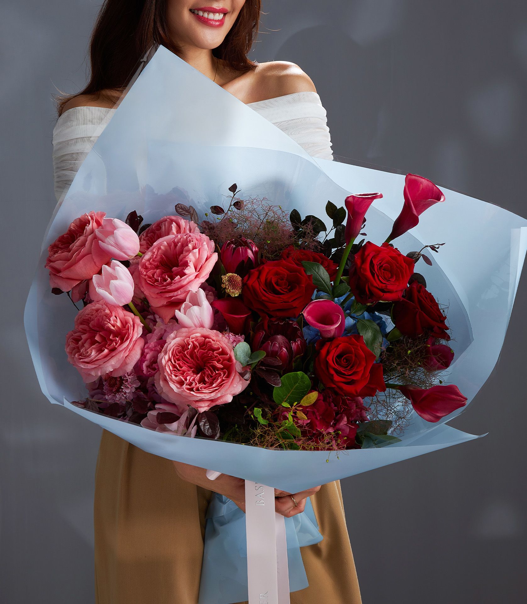 Woman holding a luxury bouquet of pink X-pression roses, red Explorer roses, red calla lilies, tulips, and scabiosa