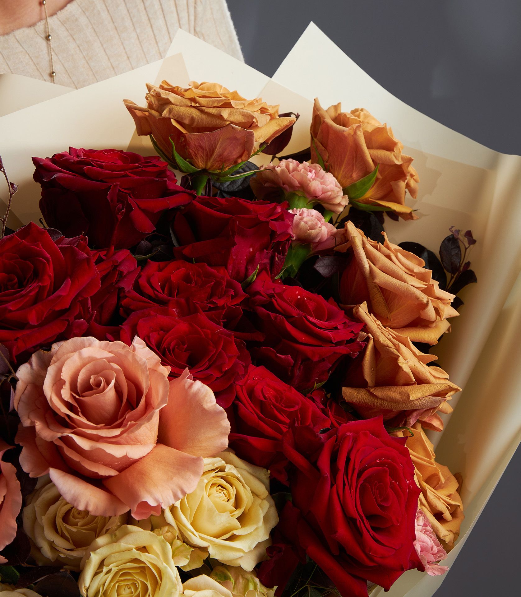 Luxurious bouquet of toffee roses, red Explorer roses, RP Moab roses, spray roses, and carnations with elegant foliage.