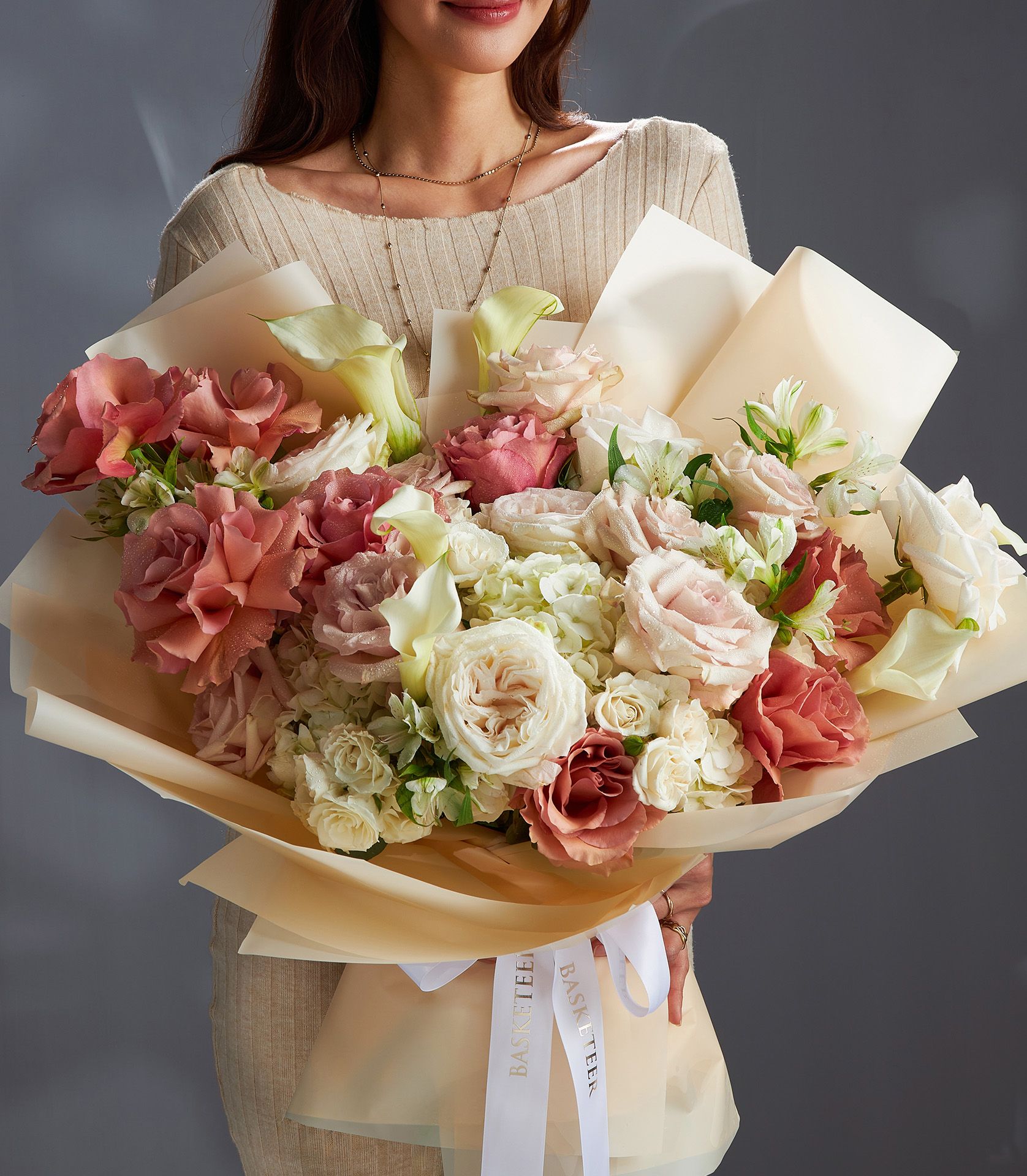 Elegant bouquet of Quicksand, White O’Hara, and RP Moab roses with white calla lilies and hydrangeas wrapped in soft beige paper.
