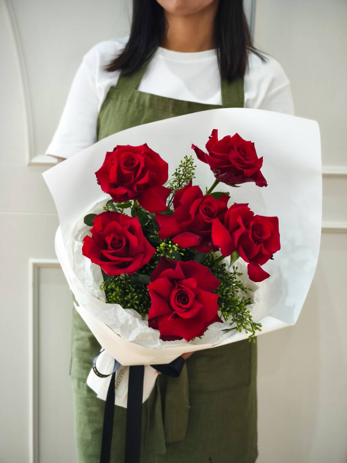 Romantic bouquet of fresh red roses with greenery, wrapped in white paper with black ribbon