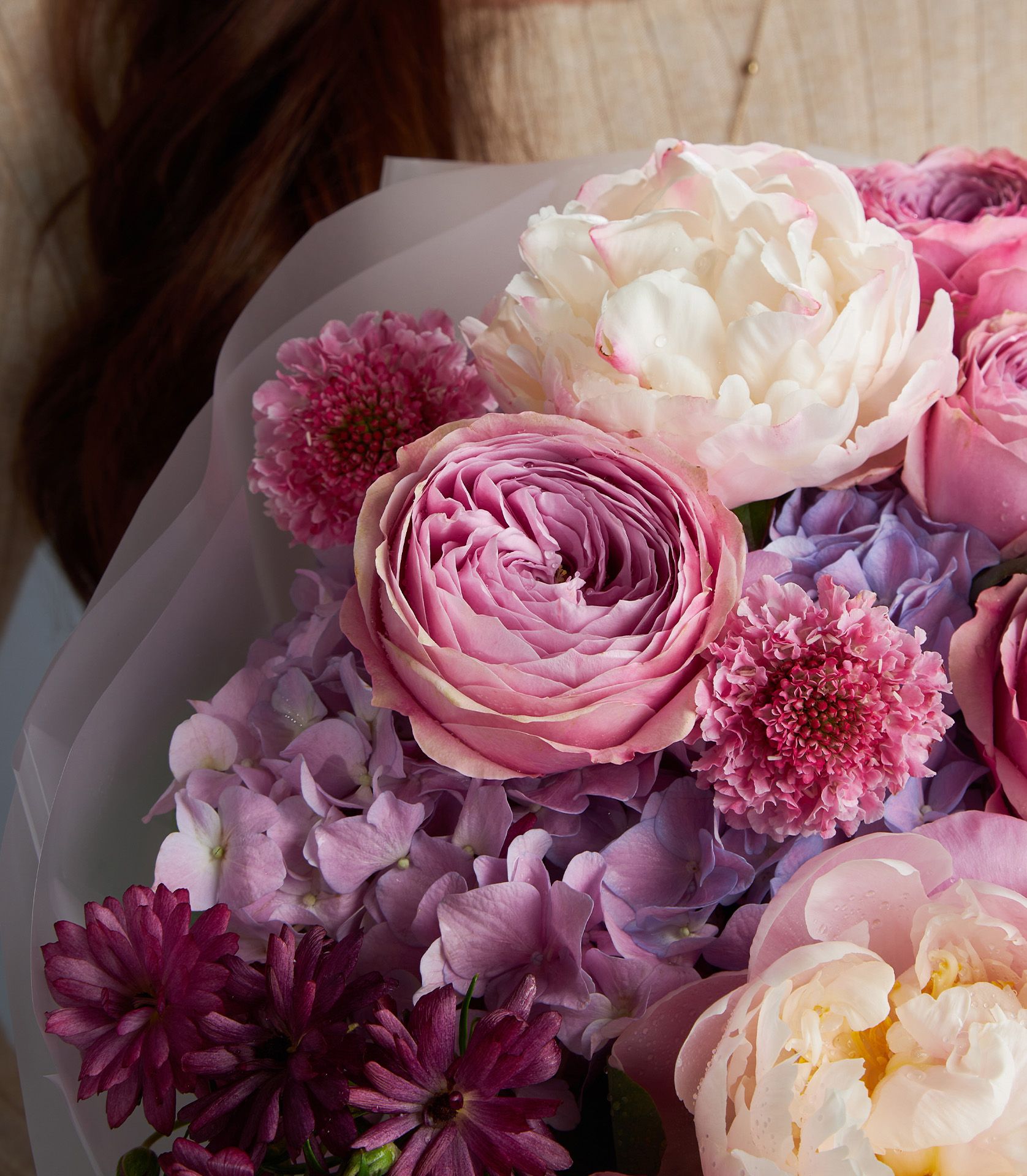 A luxurious bouquet with Peonikiss roses, white peonies, butterfly ranunculus, purple hydrangeas, and scabiosa in soft purple tones.