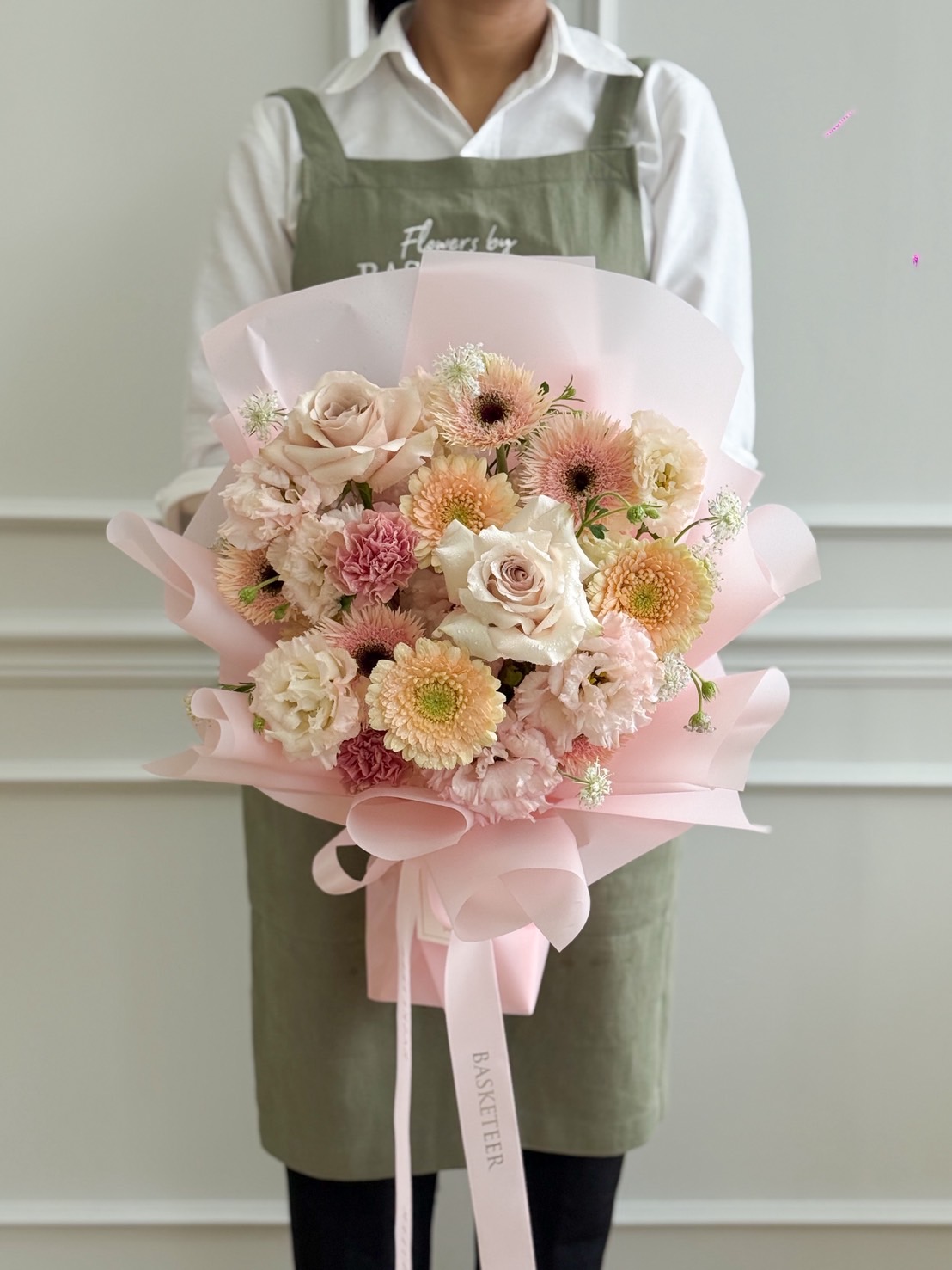 Pastel pink flower bouquet with roses, carnations, gerberas, and lisianthus, wrapped in pink paper with satin ribbon.