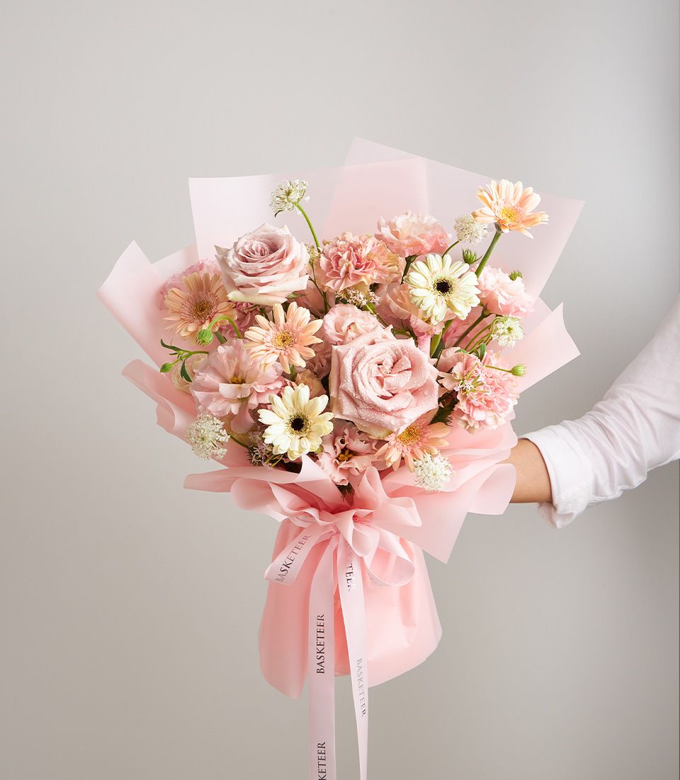 A delicate bouquet of pink roses, gerberas, carnations, and white scabiosa, wrapped in soft pink paper with a satin ribbon.