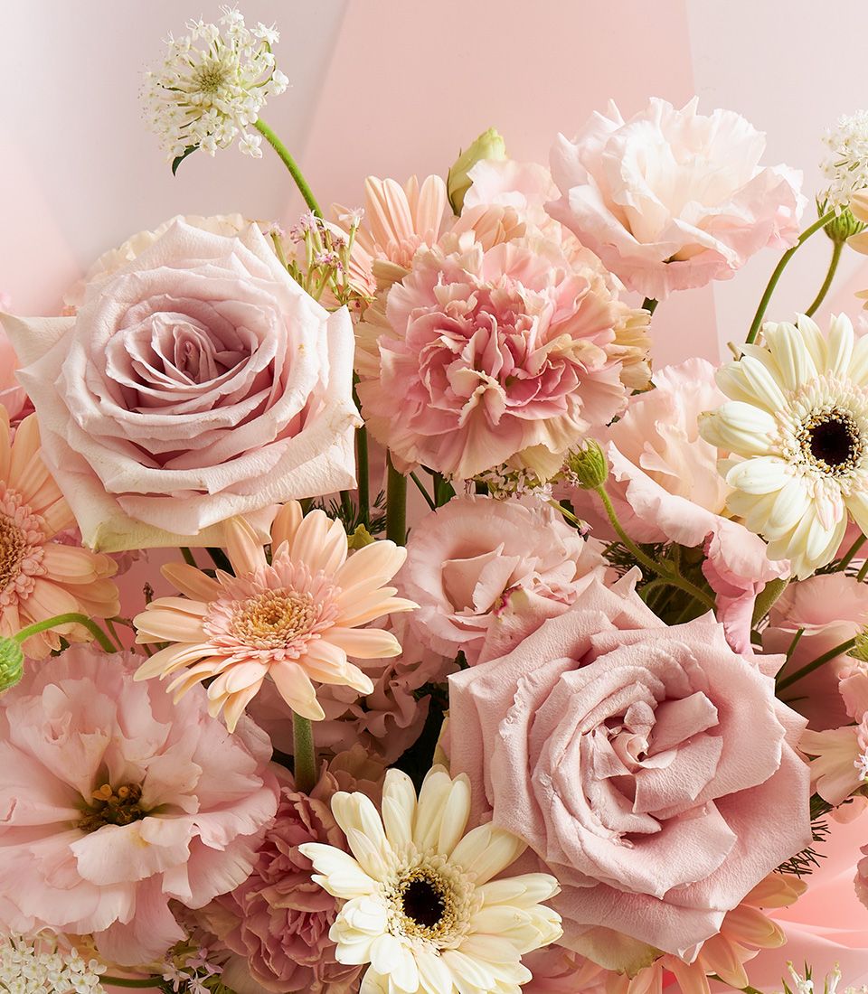 A pastel bouquet of pink roses, cream gerberas, carnations, and lisianthus, arranged for a soft and romantic look.