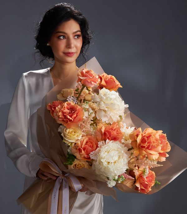 Luxurious bouquet with vibrant orange roses, white peonies, yellow roses, white hydrangeas, and blush astilbe in warm earthy tones.