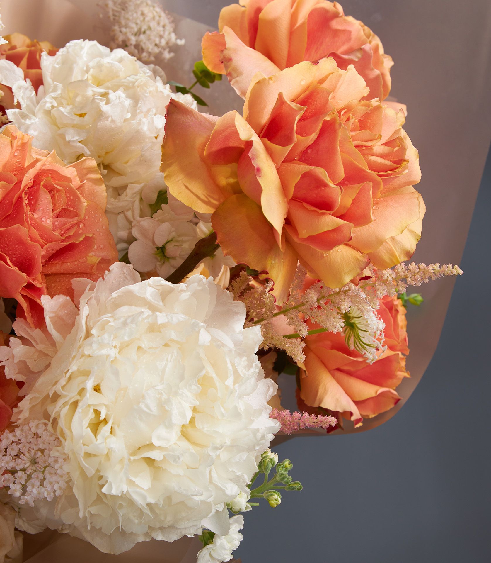 Close-up of orange roses with dewdrops and white peonies, accented with blush astilbe for a fresh, romantic look.