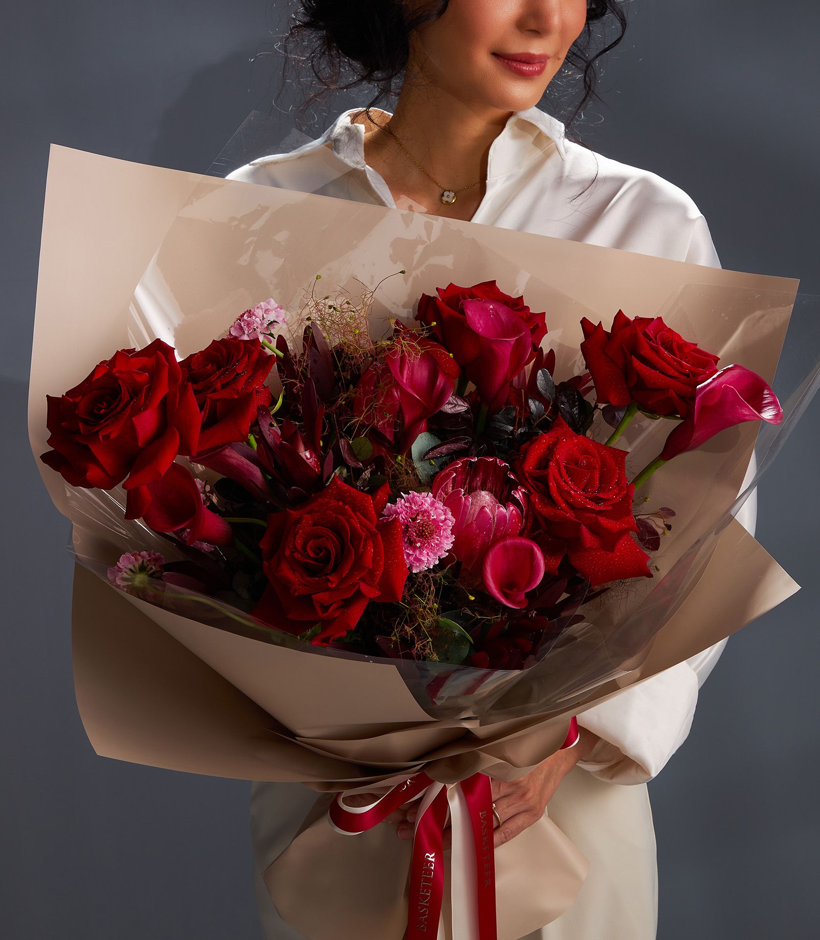 Elegant bouquet featuring Explorer red roses, red calla lilies, pink scabiosa, red protea flowers, burgundy eucalyptus, and cotinus foliage.