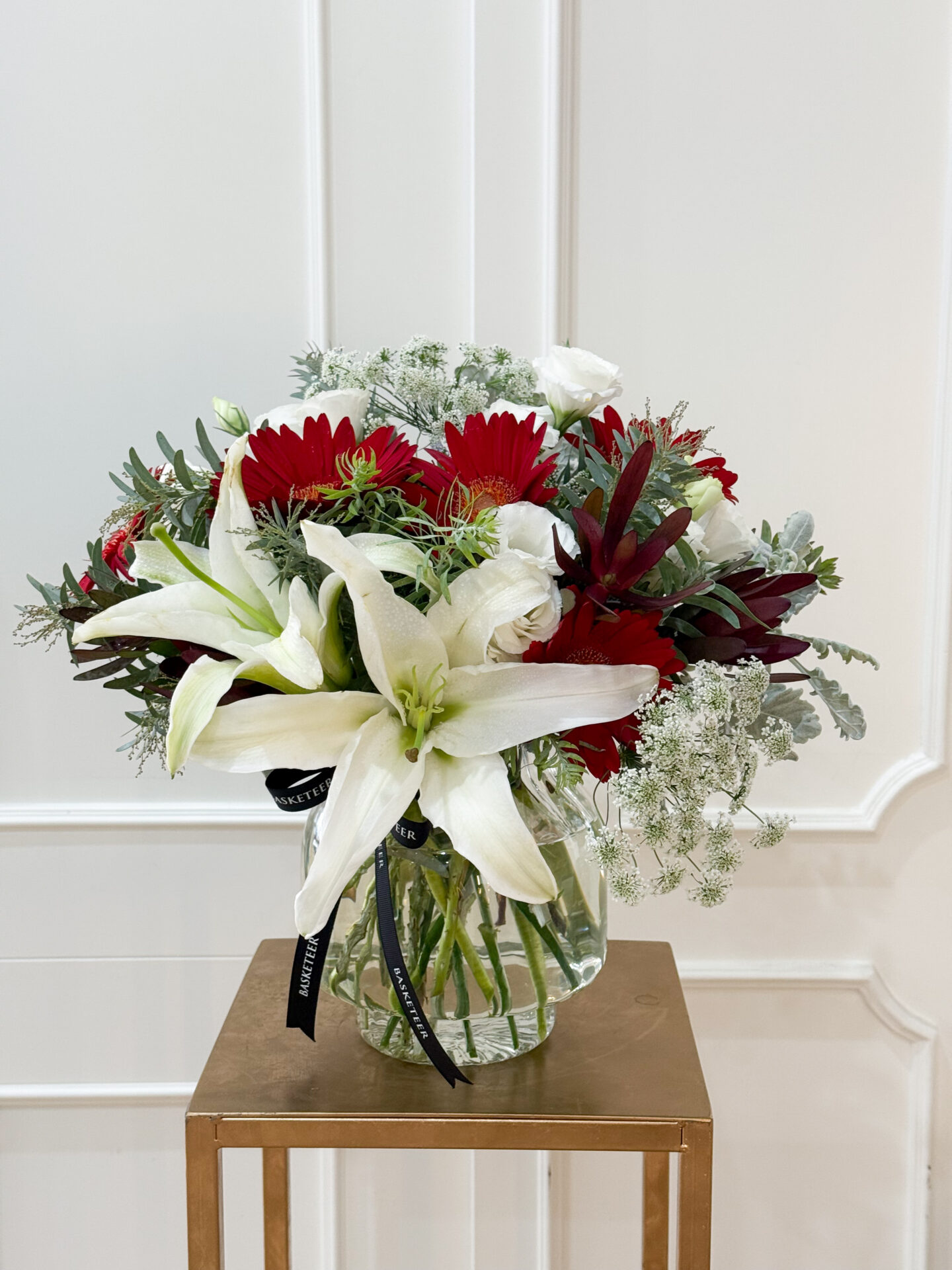 Luxury glass vase with white lilies, red gerberas, lisianthus, queen anne’s lace, and elegant greenery accents.