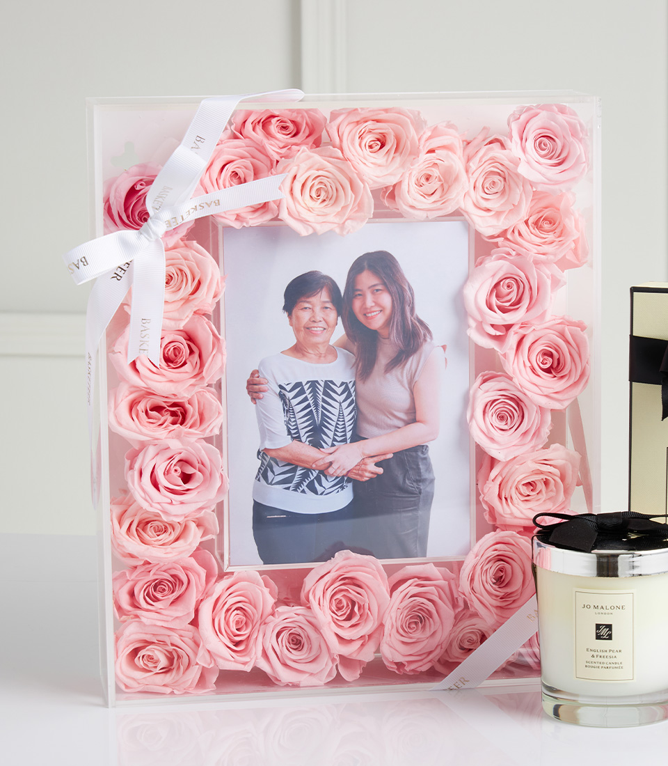 Close-up of a pink rose photo frame with a mother and daughter picture, tied with a white ribbon, next to a Jo Malone scented candle.