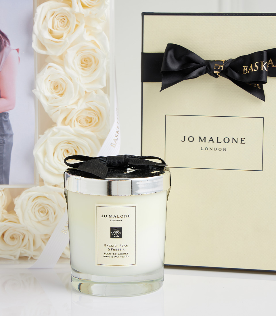 Close-up of Jo Malone London English Pear & Freesia scented candle with black bow, white rose frame, and Jo Malone gift box.