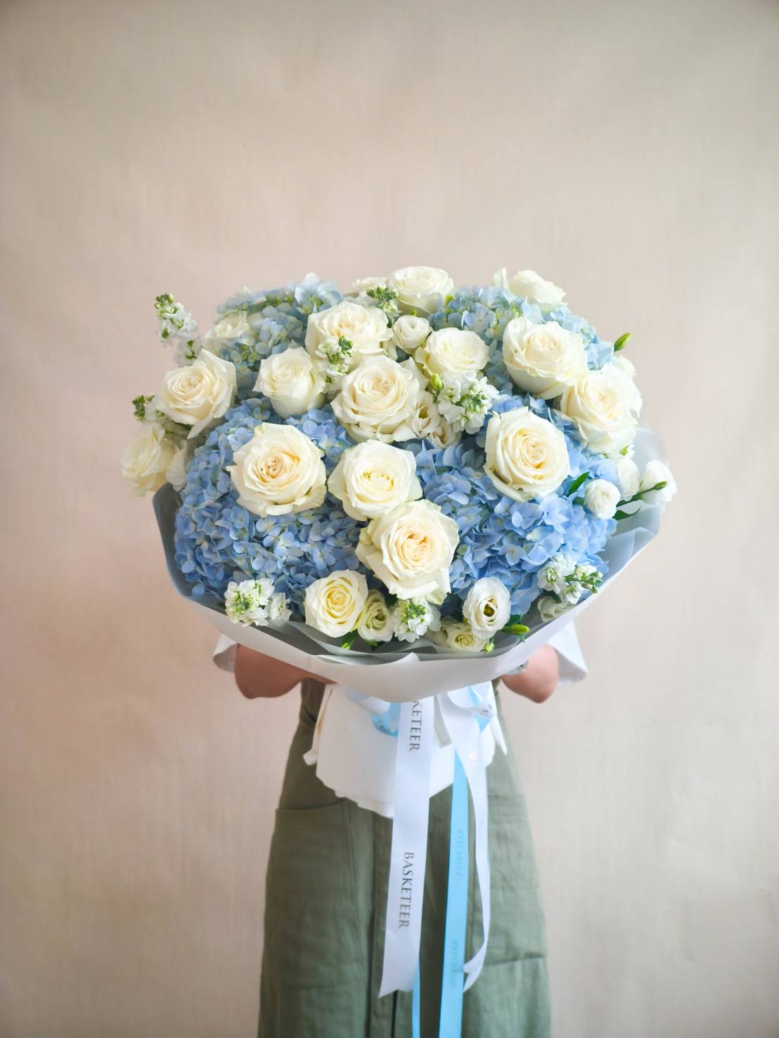 Luxury bouquet of white roses and blue hydrangeas with white blooms, wrapped in elegant white paper and blue ribbon.