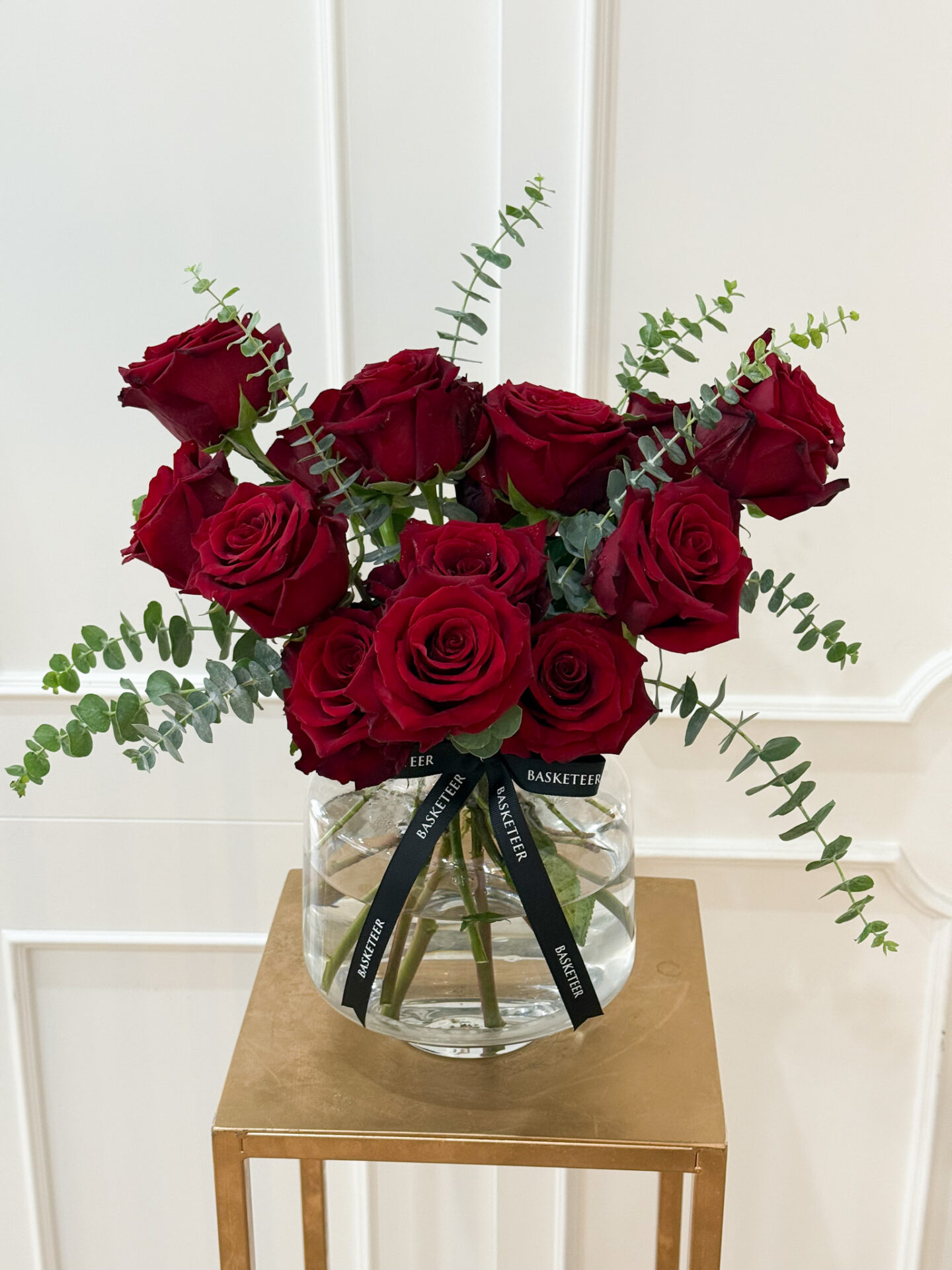Elegant vase with premium red roses and eucalyptus greenery tied with a black Basketeer ribbon.
