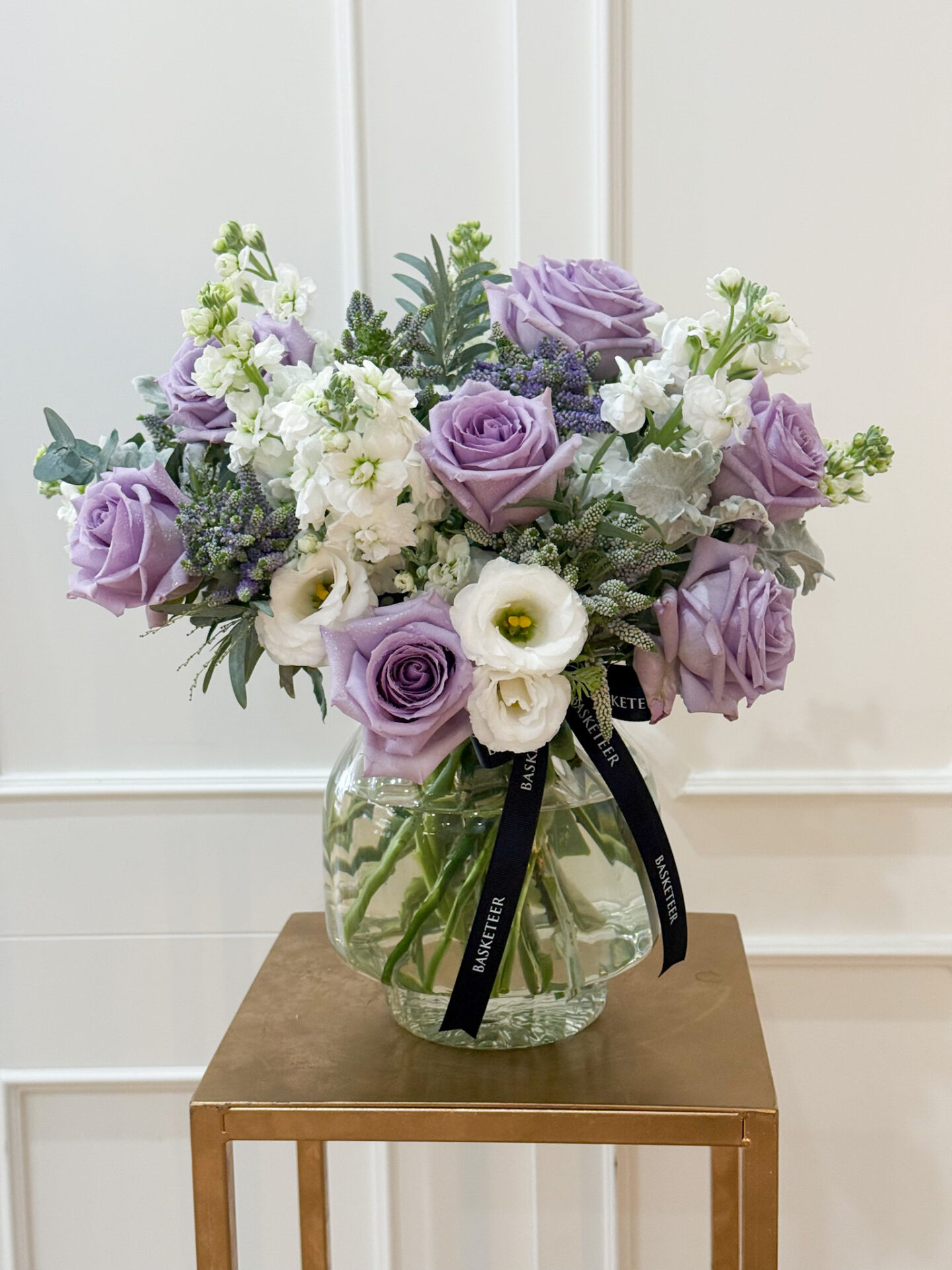 Luxury vase with lavender roses, white lisianthus, and delicate white stock, tied with Basketeer ribbon.