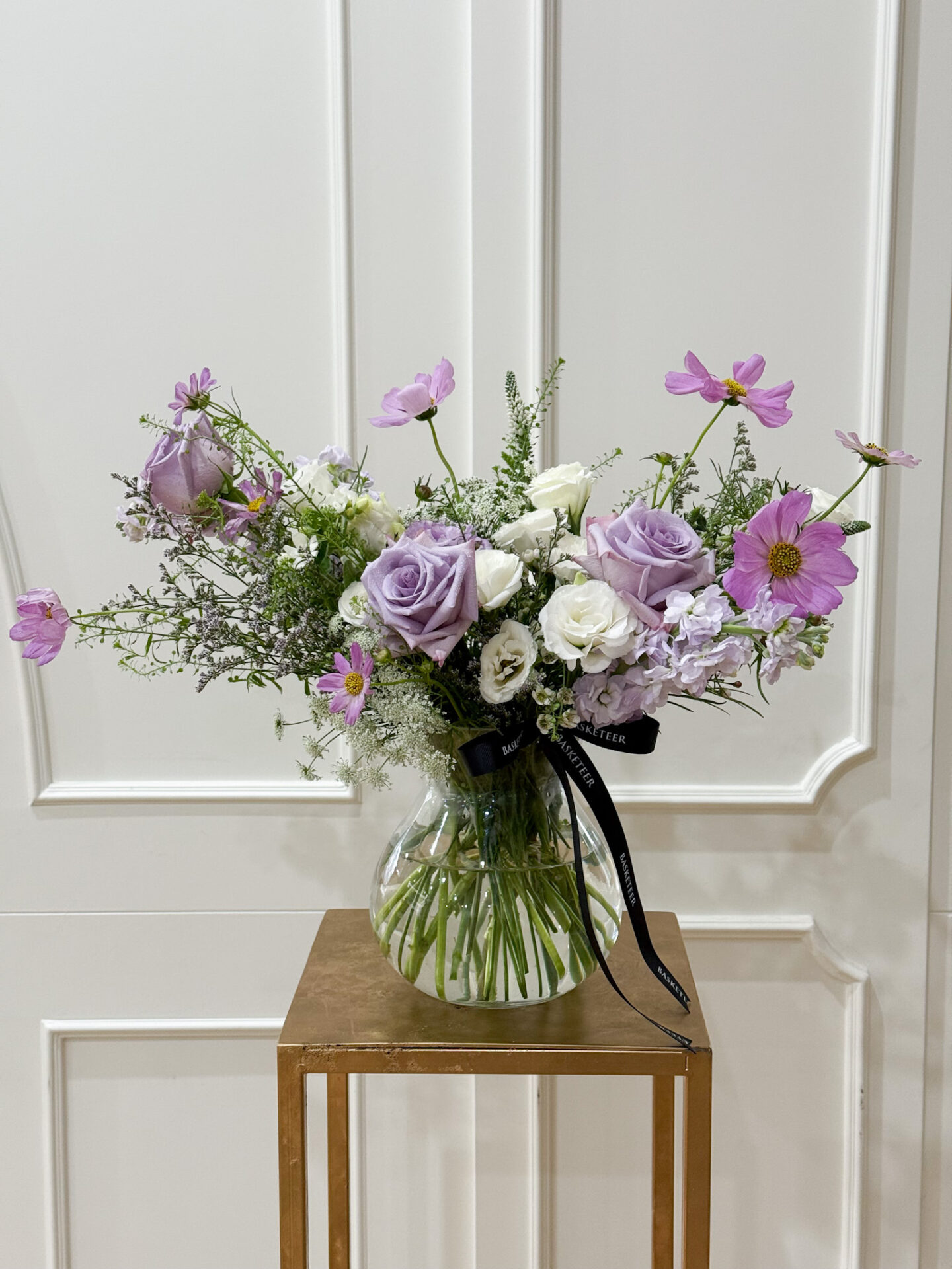 Glass vase arrangement with lavender roses, pink cosmos, white lisianthus, and seasonal fillers in a soft romantic style.
