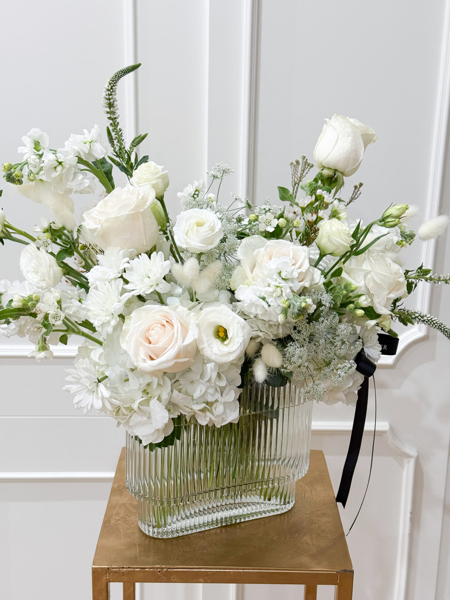 Glass vase with ivory roses, white hydrangeas, lisianthus, and delicate fillers for a pure elegant design.