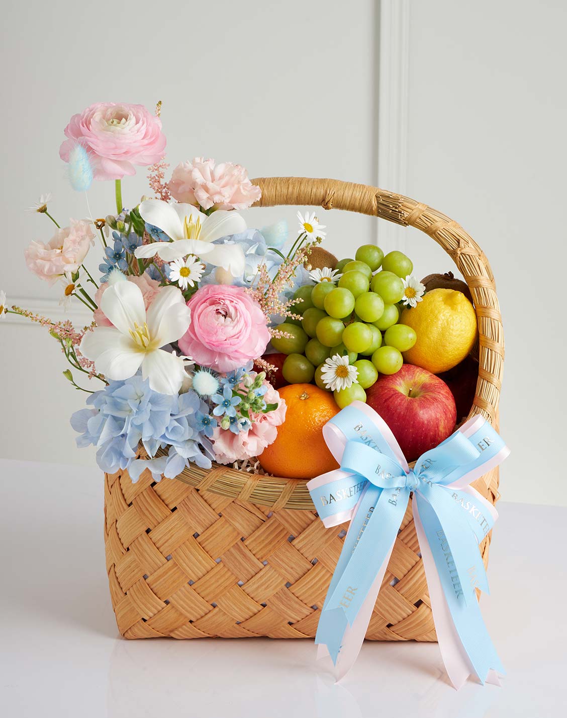 Luxury fruit and flower gift basket with pastel blooms including lilies, ranunculus, hydrangeas, and fresh seasonal fruits