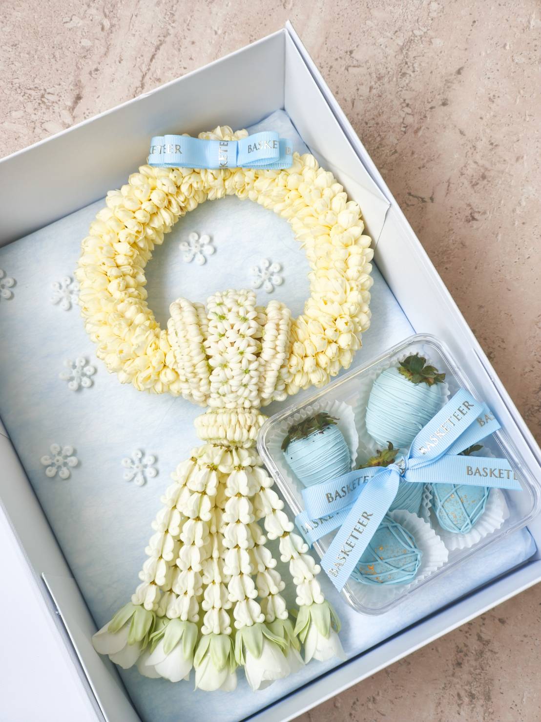 Premium cream jasmine garland with white rose buds and a set of blue chocolate-covered strawberries, tied with pastel blue “Basketeer” ribbons in a luxury gift box.