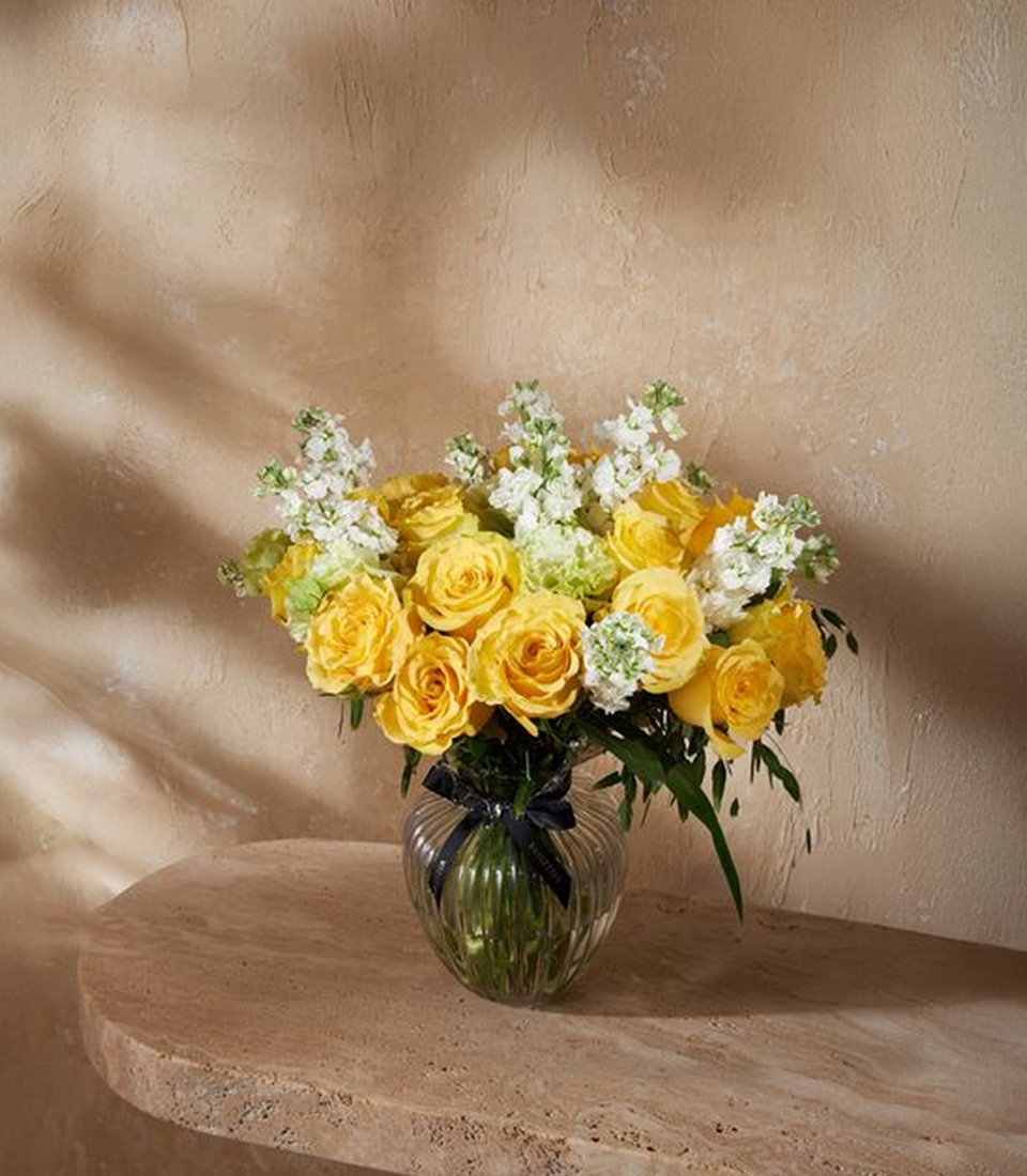 Luxury vase arrangement with vibrant yellow roses, white stock, and greenery for a cheerful and elegant floral design.
