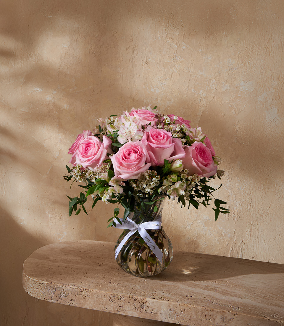 Elegant glass vase with pink roses, white flowers, and greenery, styled in a luxury floral arrangement.