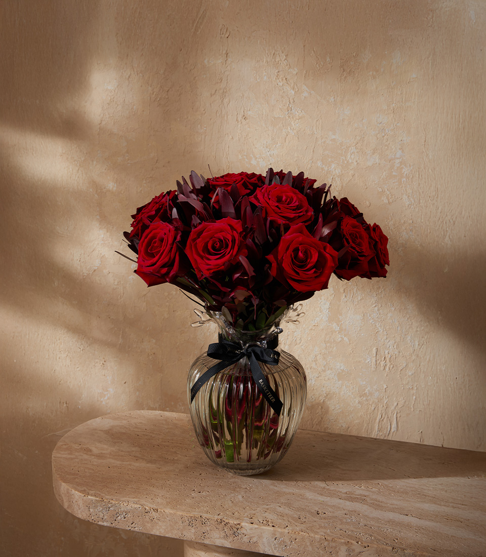 Elegant vase arrangement of premium red roses with dark foliage, tied with a black satin ribbon.