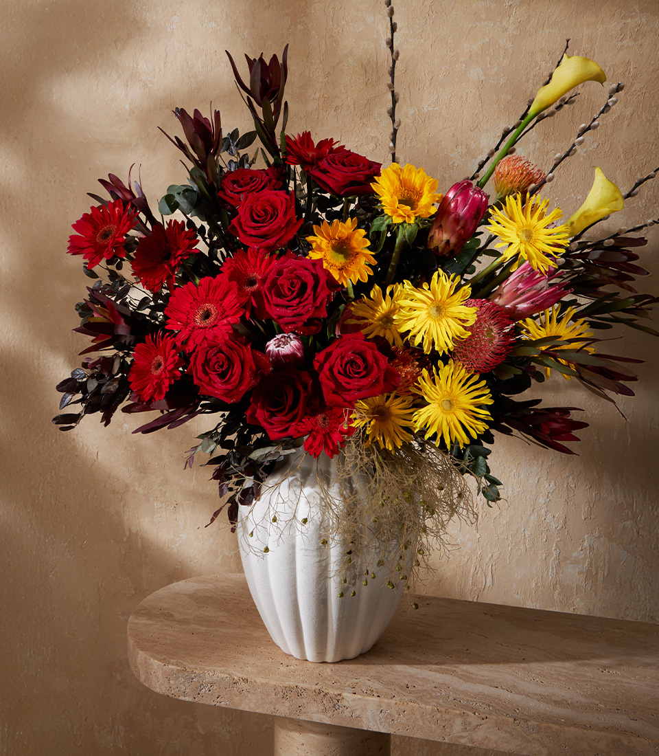 Bold vase arrangement with red roses, yellow gerbera, calla lilies, and protea – luxury flower delivery Bangkok.