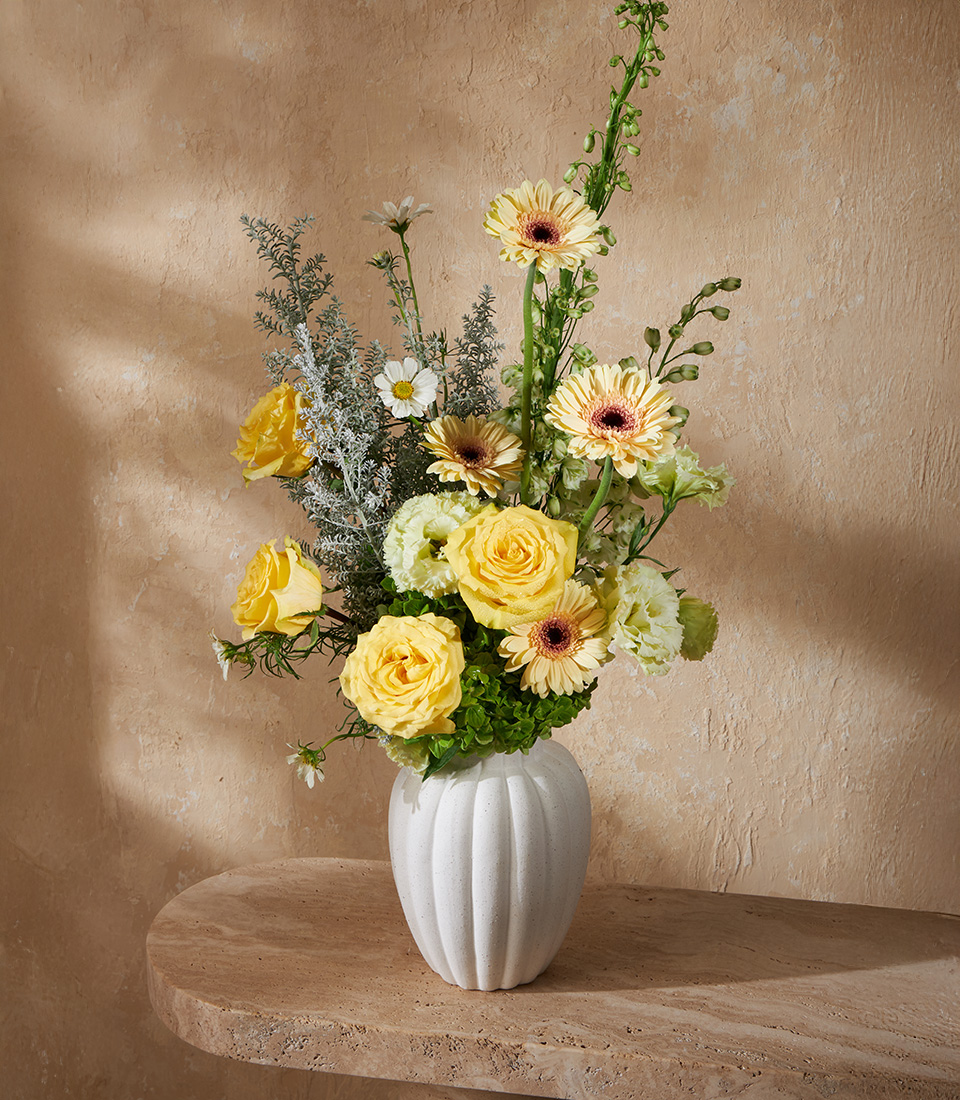Cheerful flower arrangement with yellow roses, gerbera daisies, and chamomile in a white vase, perfect for joyful gifts and Bangkok flower delivery.