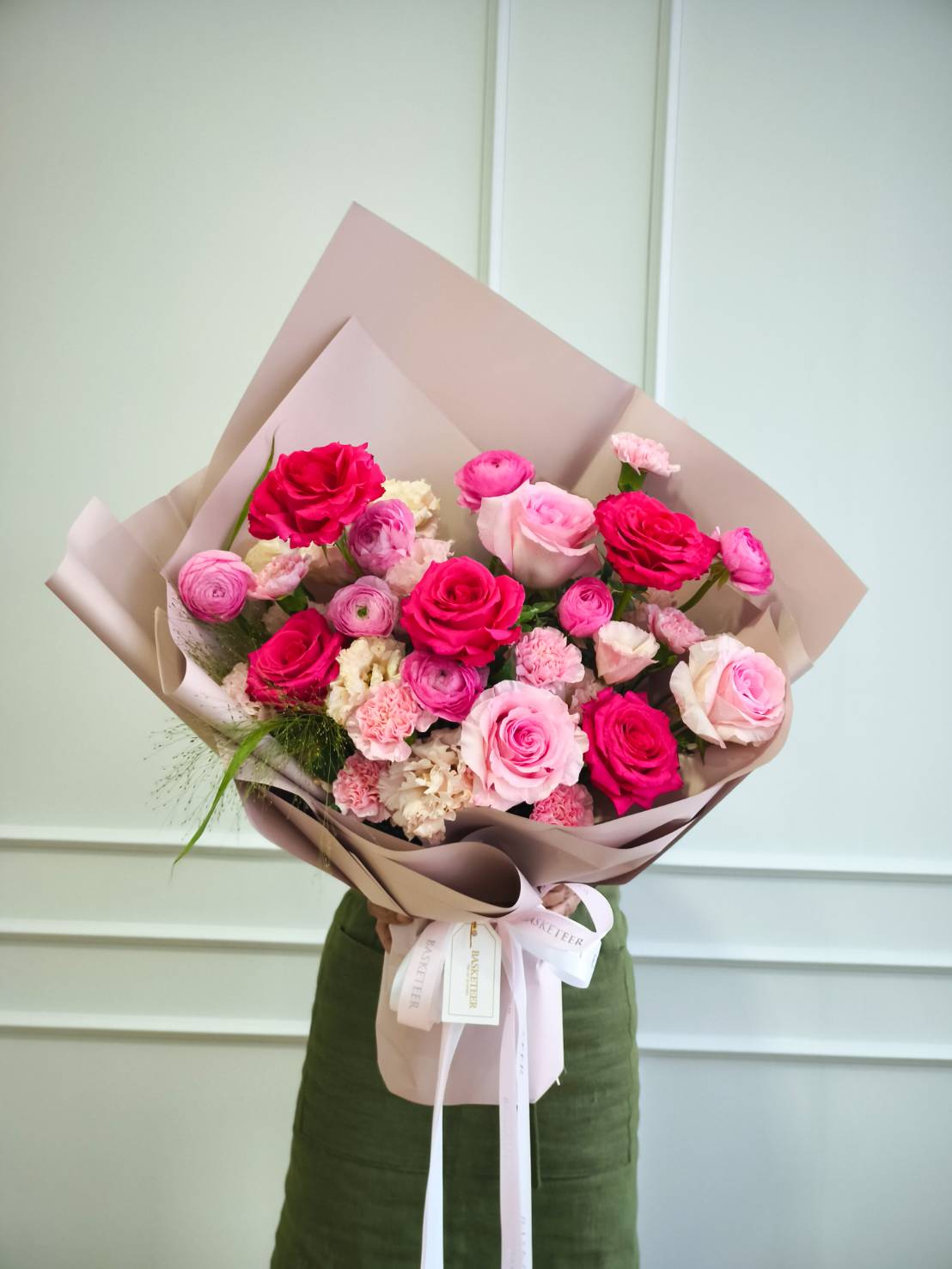 Luxury bouquet of pink and red roses with ranunculus and carnations, wrapped in nude paper, tied with a white satin ribbon
