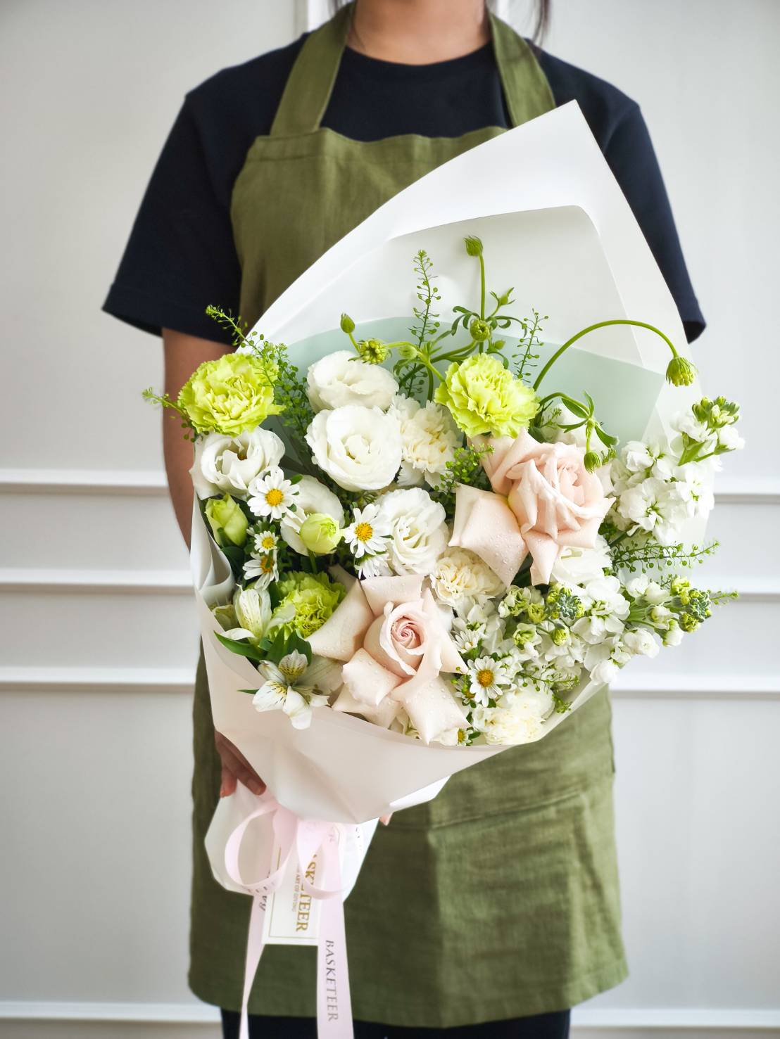 Elegant bouquet with white roses, green carnations, chamomile daisies, and lisianthus wrapped in white paper with pink ribbon