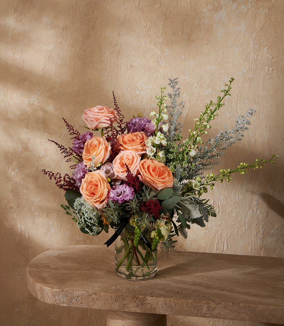 Elegant vase arrangement of peach roses purple lisianthus red astilbe and queen anne lace with greenery accents