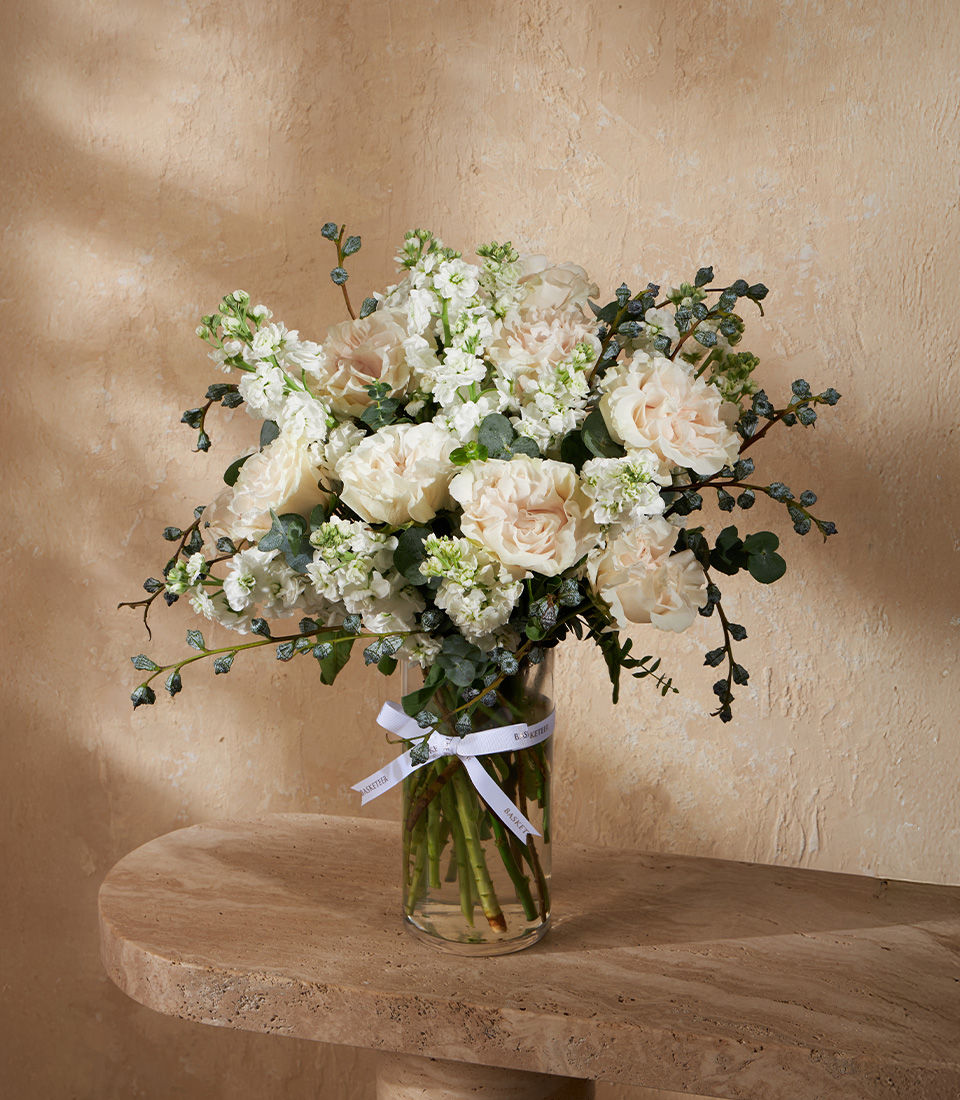 Flower arrangement with white and cream roses, stock flowers, and eucalyptus in a clear vase – Bangkok delivery.