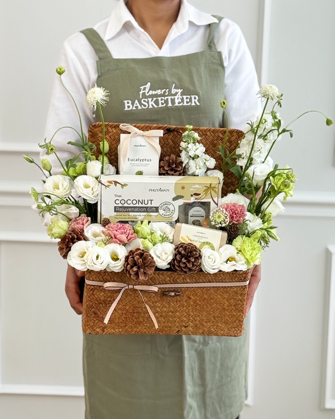 Natural woven basket with Phutawan spa products, decorated with white lisianthus, carnations, hydrangeas, and pinecones.