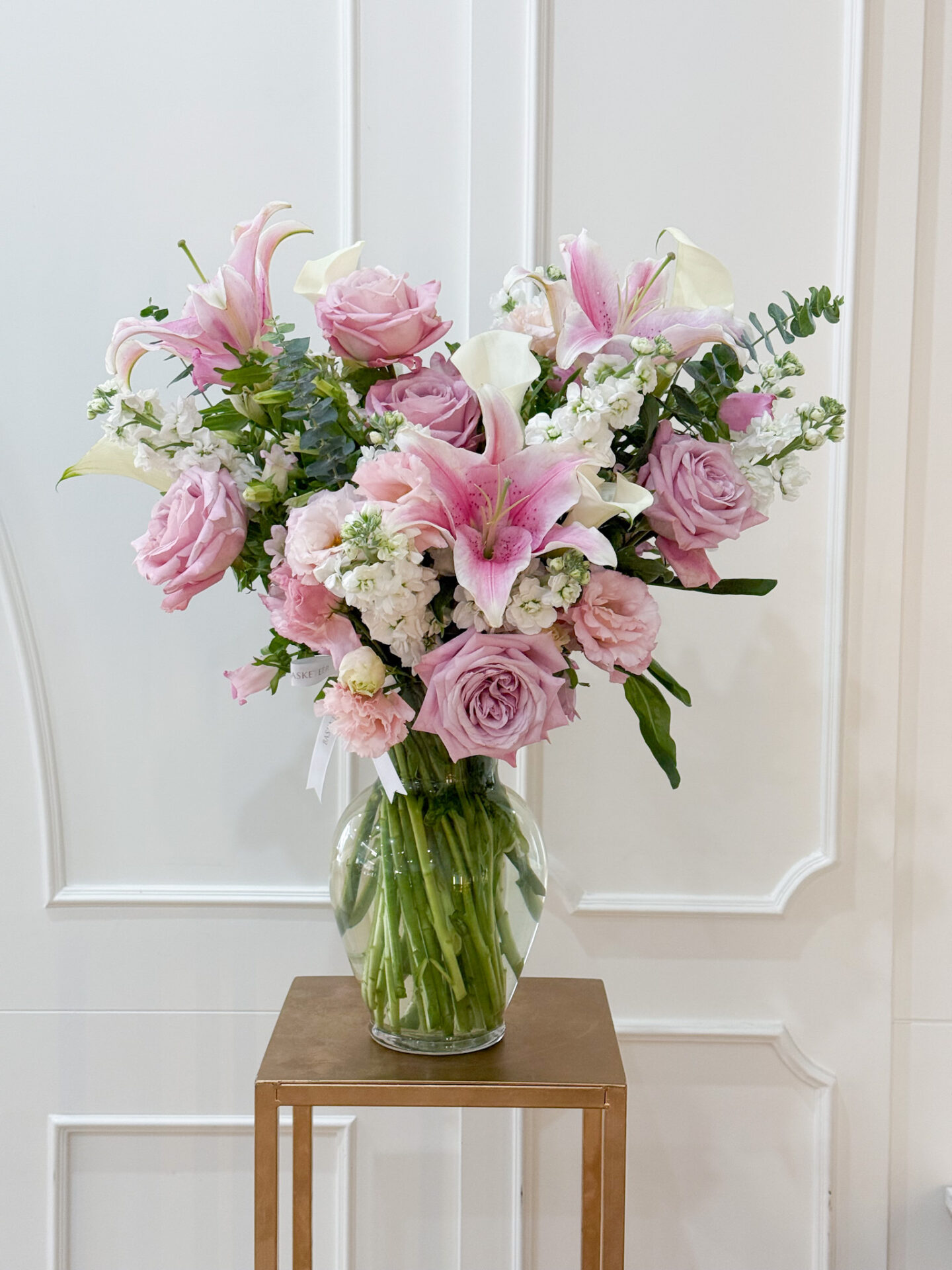 Elegant glass vase arrangement with pink lilies, pastel roses, white calla lilies, and delicate fillers, creating a soft romantic display.