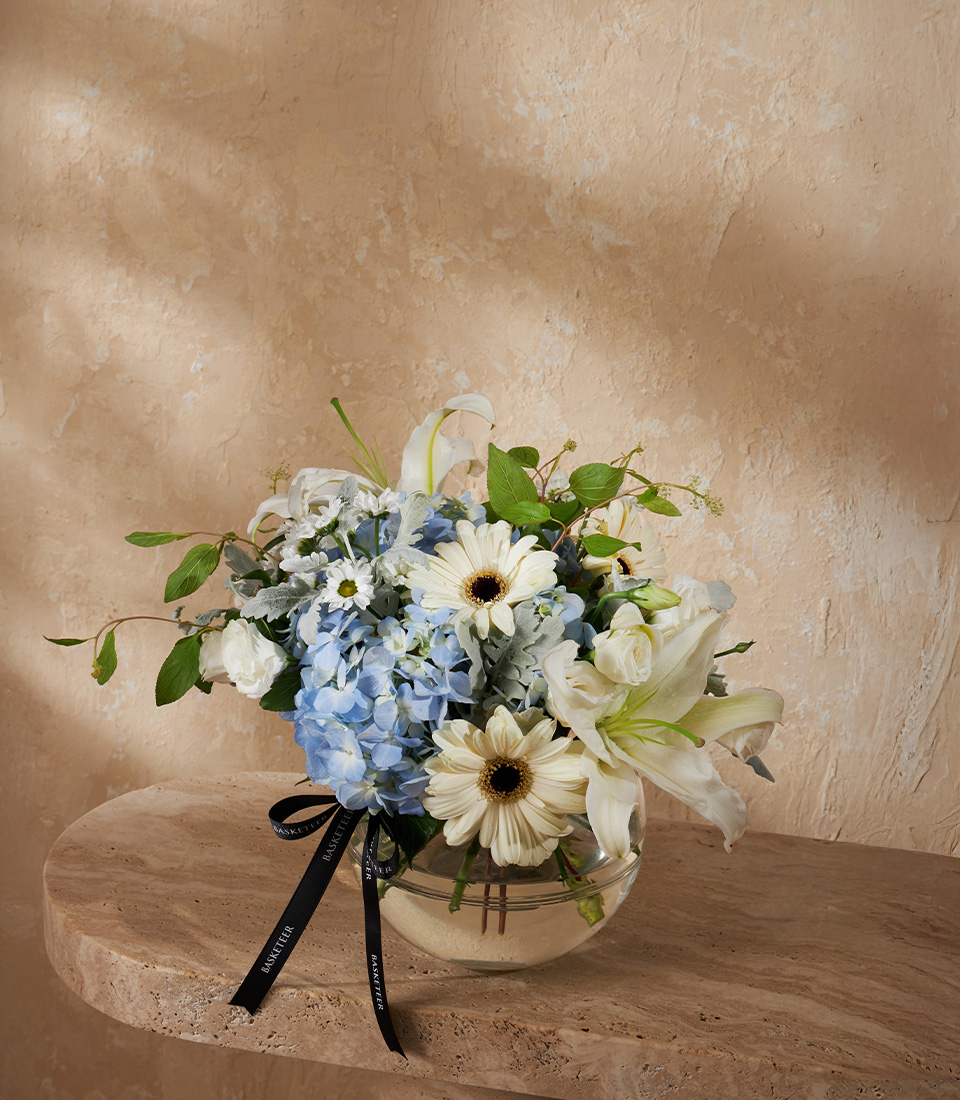 Flower vase arrangement with blue hydrangeas white gerberas and lilies in a clear round vase