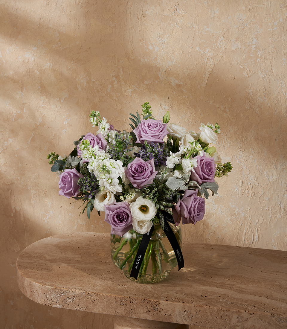 Flower vase arrangement with purple roses white flowers and greenery in a round clear vase