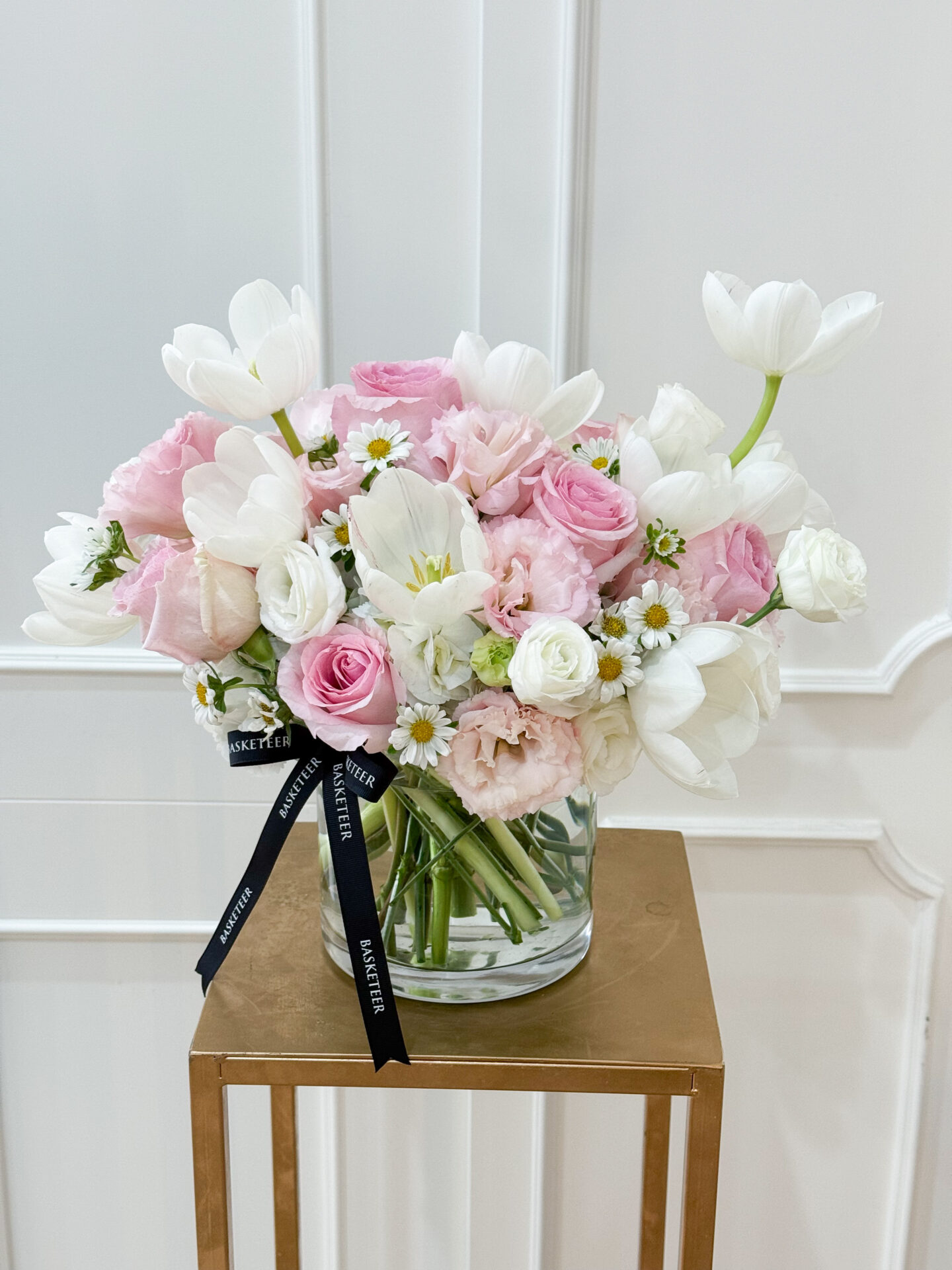 Elegant vase arrangement with pink roses, white tulips, chamomile, and soft pink lisianthus, styled in a clear glass vase with black satin ribbon.