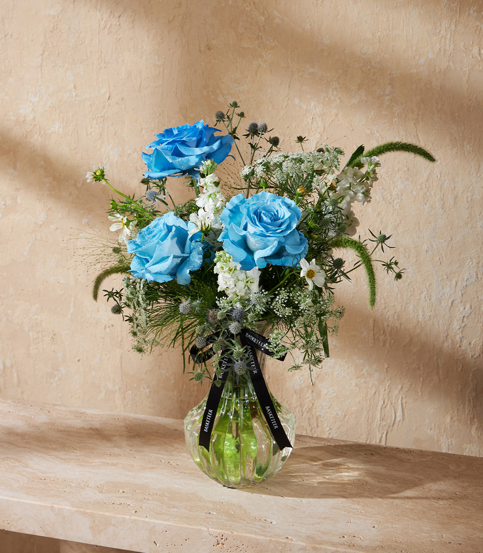 Vase arrangement with premium blue roses white accent flowers and fresh greenery in a clear glass vase Unique bouquet for flower delivery in Bangkok