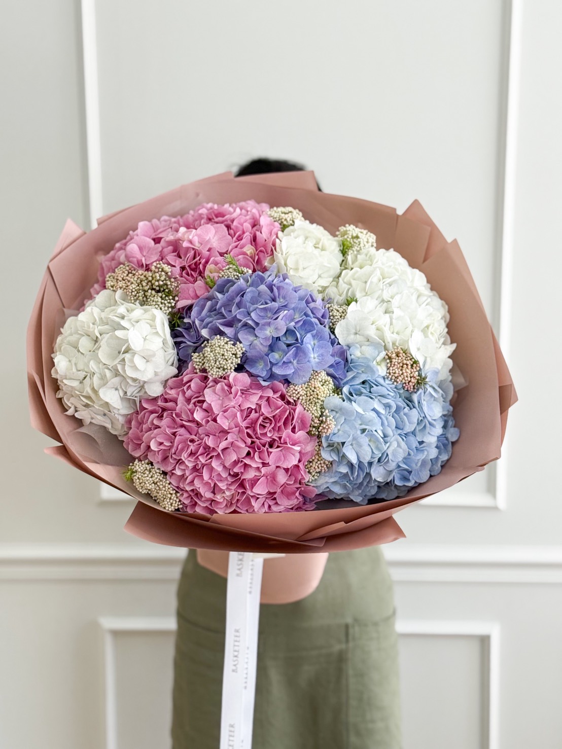 Luxury bouquet of pastel hydrangeas in pink, blue, purple, and white, wrapped in nude pink paper.