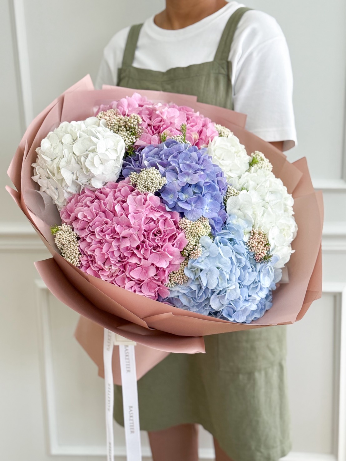 Large pastel hydrangea bouquet in pink, blue, purple, and white, wrapped in elegant nude pink paper.
