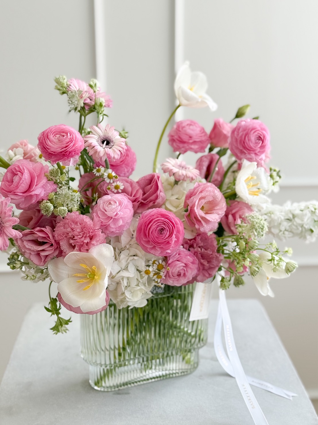 Elegant vase with pink ranunculus, gerbera, carnations, lisianthus, white tulips, and hydrangeas, arranged in a clear glass vase for delivery in Bangkok