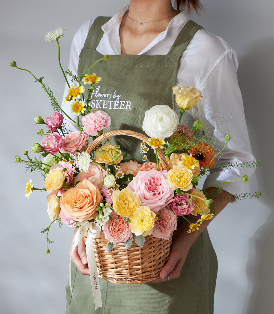 Flower basket with peach roses pink garden roses yellow spray roses chamomile and seasonal blooms arranged in a woven basket for luxury flower delivery in Bangkok