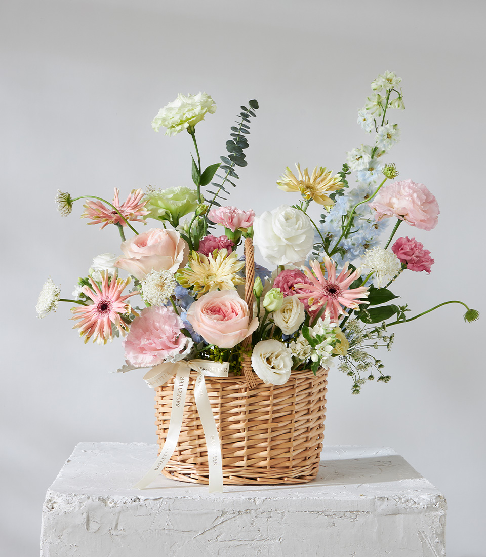 Pastel flower arrangement basket with pink roses white ranunculus yellow gerberas and blue delphiniums for premium delivery in Bangkok